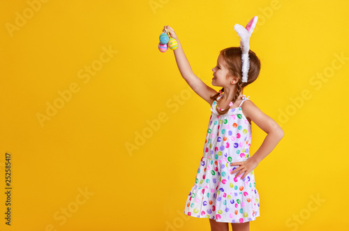 funny happy child girl with easter eggs on yellow.