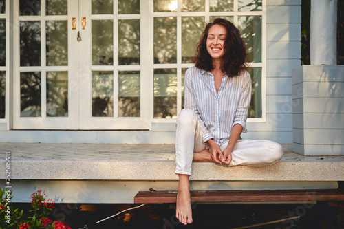 Portrait of a beautiful happy young woman sitting on the porch of terrace with her house on background