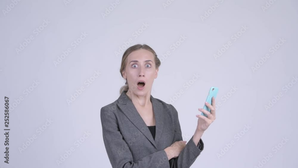 Happy young blonde businesswoman using phone and looking surprised Happy young blonde businesswoman using phone and looking surprised