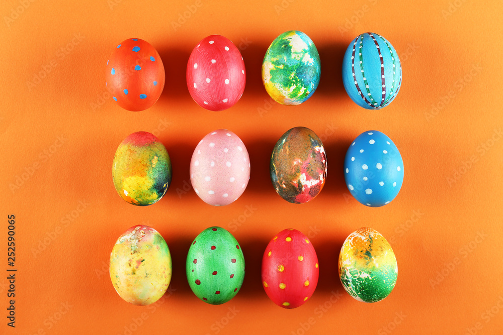 Bunch of colorful tie dye and polka dot painted Easter eggs on bright orange paper background with a lot of copy space for text. Top view, flat lay, close up. Easter greeting card concept.