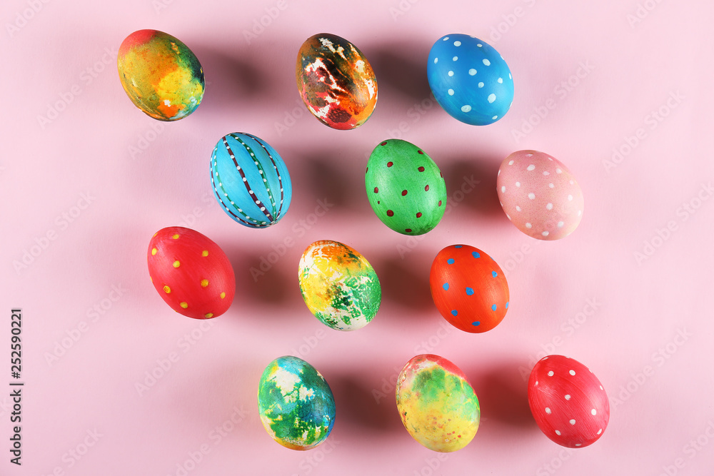 Bunch of colorful tie dye and polka dot painted Easter eggs on pale pink paper background with a lot of copy space for text. Top view, flat lay, close up. Easter greeting card concept. Bunch of colorful tie dye and polka dot painted Easter eggs on pale pink paper background with a lot of copy space for text. Top view, flat lay, close up. Easter greeting card concept.