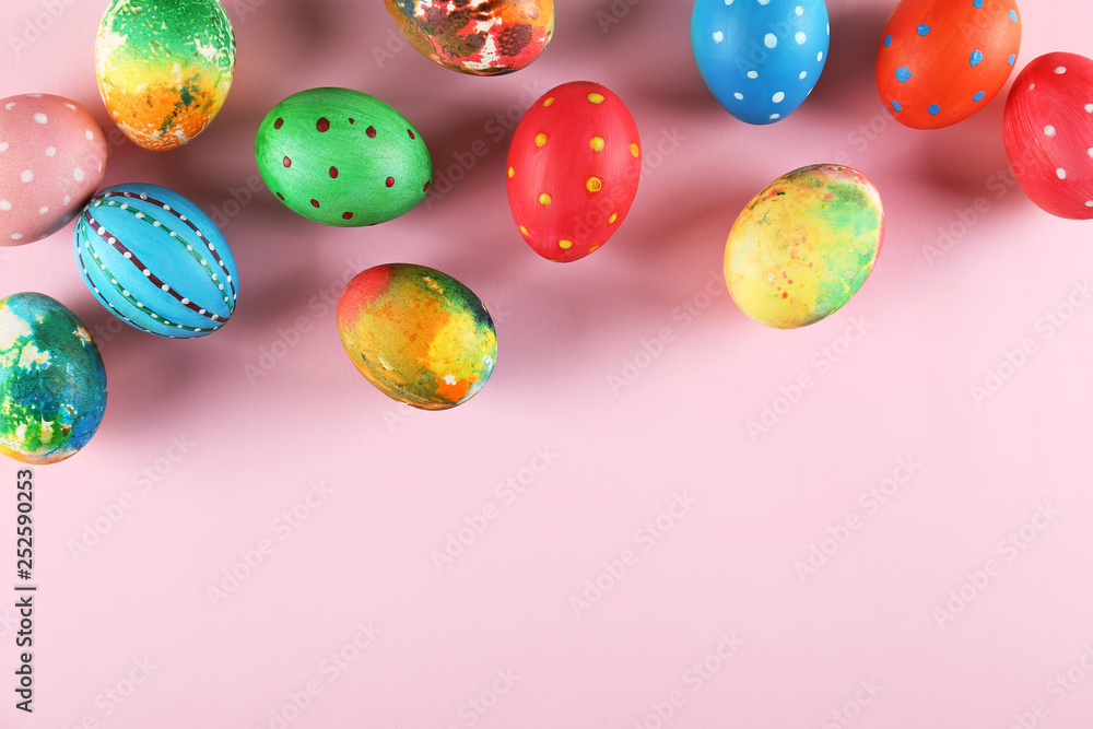 Bunch of colorful tie dye and polka dot painted Easter eggs on pale pink paper background with a lot of copy space for text. Top view, flat lay, close up. Easter greeting card concept.