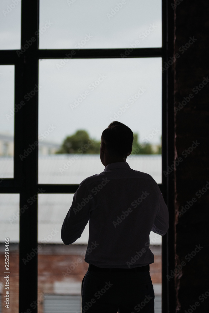 Morning of the groom. Room in loft style. Big windows. The groom wears a shirt, a tie. Morning of the groom. Room in loft style. Big windows. The groom wears a shirt, a tie.
