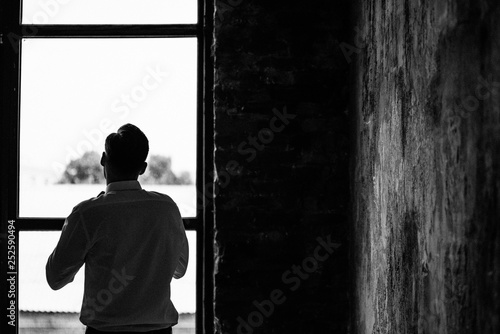 Morning of the groom. Room in loft style. Big windows. The groom wears a shirt, a tie. Black and white photo