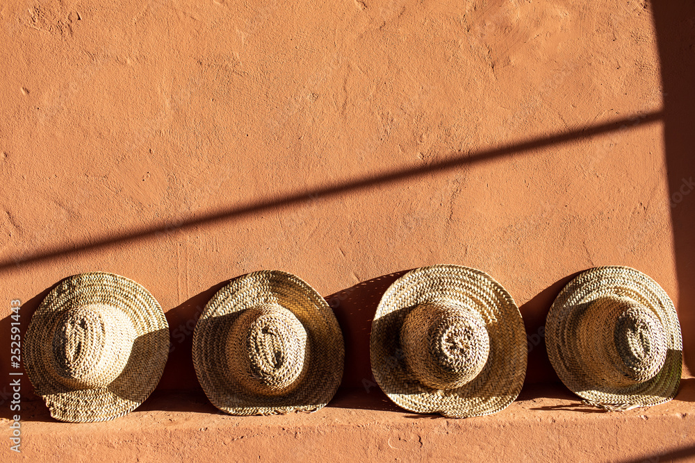 Straw beach hats standing on terracotta clay wall. Bright sunlight and hard shadows.