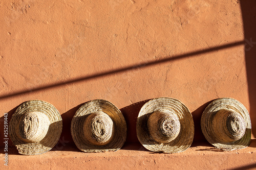 Straw beach hats standing on terracotta  clay wall.  Bright sunlight and hard shadows.