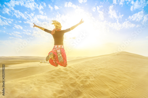 Inland sea landscape, a major tourist destination for Qatar. Woman traveler jumping on sand dunes in Qatar desert at sunset. Happy caucasian tourist at Khor at Udaid in Persian Gulf, Arabian Peninsula