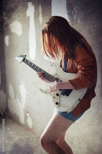 Young red-haired girl with an electric guitar. Rock musician girl in a leather jacket. She is a pretty singer and a performer of rock music.