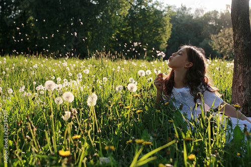 Teen blowing seeds from a dandelion flower in a spring park