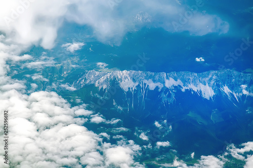 View of the Earth from the airplane flying above the clouds at high altitude over the mountains. Selective Focus