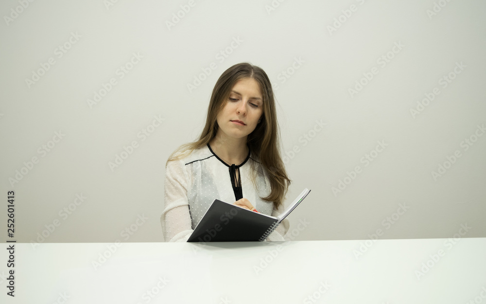 A young brunette girl with flowing hair is sitting at a table with a notebook in her hands, holding a pen in her hand, carefully and seriously writing down the diary A young brunette girl with flowing hair is sitting at a table with a notebook in her hands, holding a pen in her hand, carefully and seriously writing down the diary