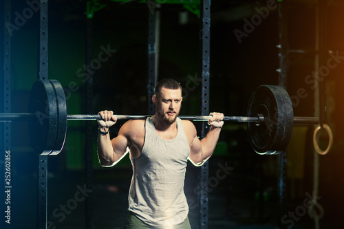 Man with heavyweight barbell in the dark gym.