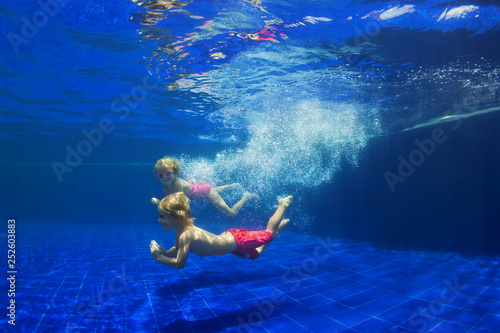 Happy family - funny kids learn to swim, dive underwater with fun. Jump with water splashes in pool. Healthy lifestyle, active people, sports activities, swimming classes on summer holidays with child