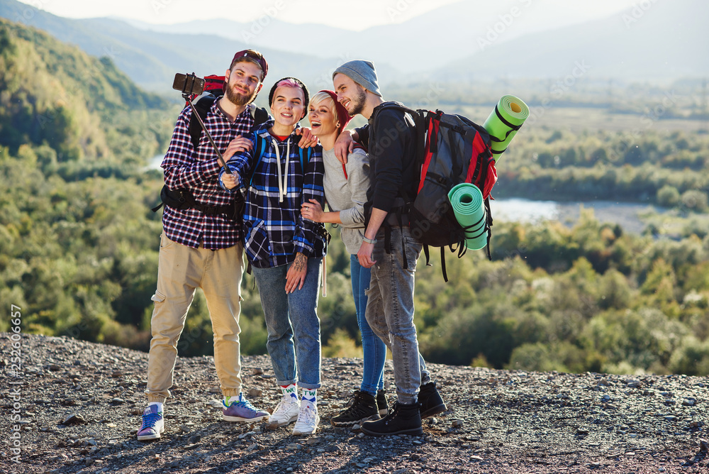 Summer travel concept. Happy friends using paper map near rented car in nature. Happy travelers in mountains on weekend vacation. Beautiful young men and women holding map, exploring location on trip.