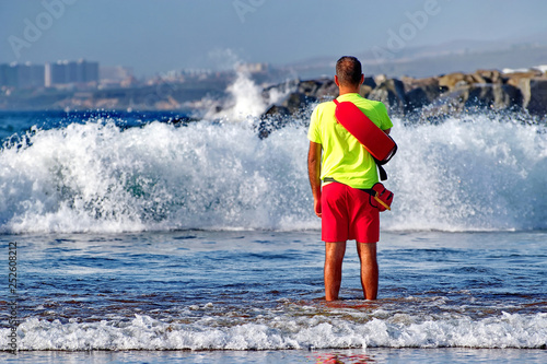 Undefined man in beach lifeguard uniform stands in the water and oversees order and the safety 