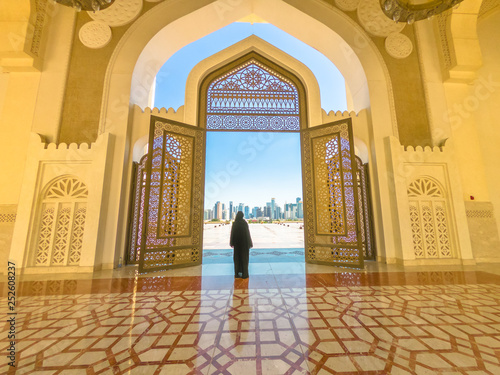 Woman with abaya dress looks at views of skyscrapers of Doha West Bay skyline outdoors State Grand Mosque in Doha, Qatar, Middle East, Arabian Peninsula. photo