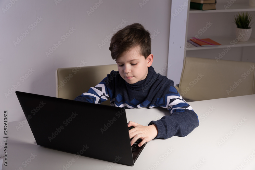 Photo of nice boy in sweater sitting infront of the computer doing homework Photo of nice boy in sweater sitting infront of the computer doing homework