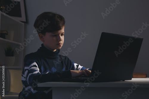 Photo of nice boy in sweater sitting infront of the computer doing homework