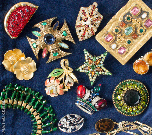 Woman's Jewelry. Vintage luxurious jewelry background. Beautiful rhinestones brooches and earrings on blue velvet background. Flat lay, top view.