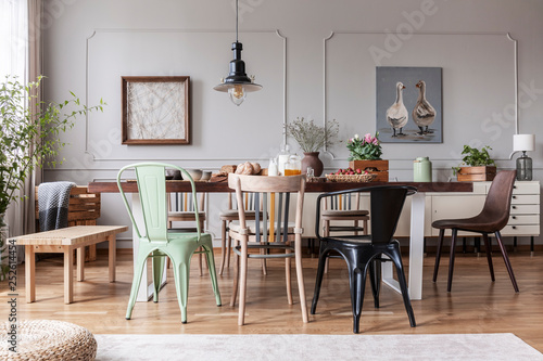 Colorful chairs at wooden table in grey rustic dining room interior with posters, flowers and table full of food, real photo photo