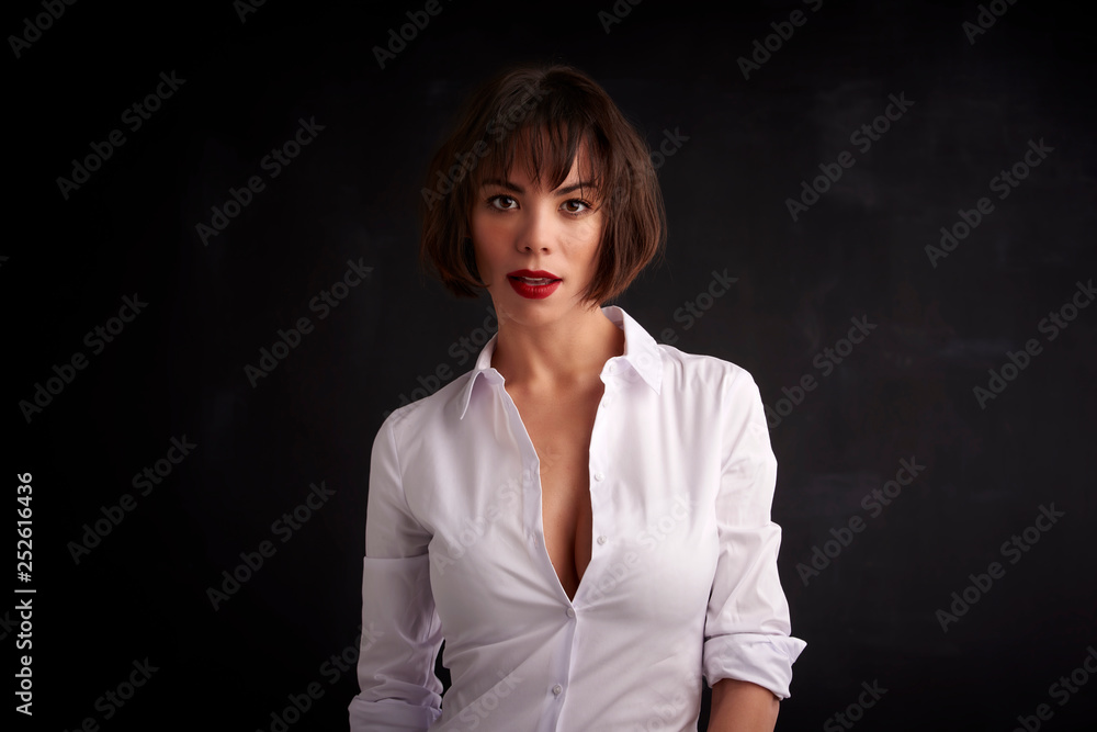 Attractive young woman wearing red lipstick and white shirt while standing at dark bakcground Attractive young woman wearing red lipstick and white shirt while standing at dark bakcground