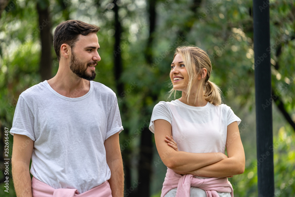 Man and Woman looking each other smiling and walking together in the public park Man and Woman looking each other smiling and walking together in the public park