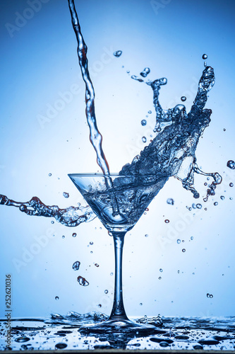 Splashing water on blue background. Cocktail glass with water.
