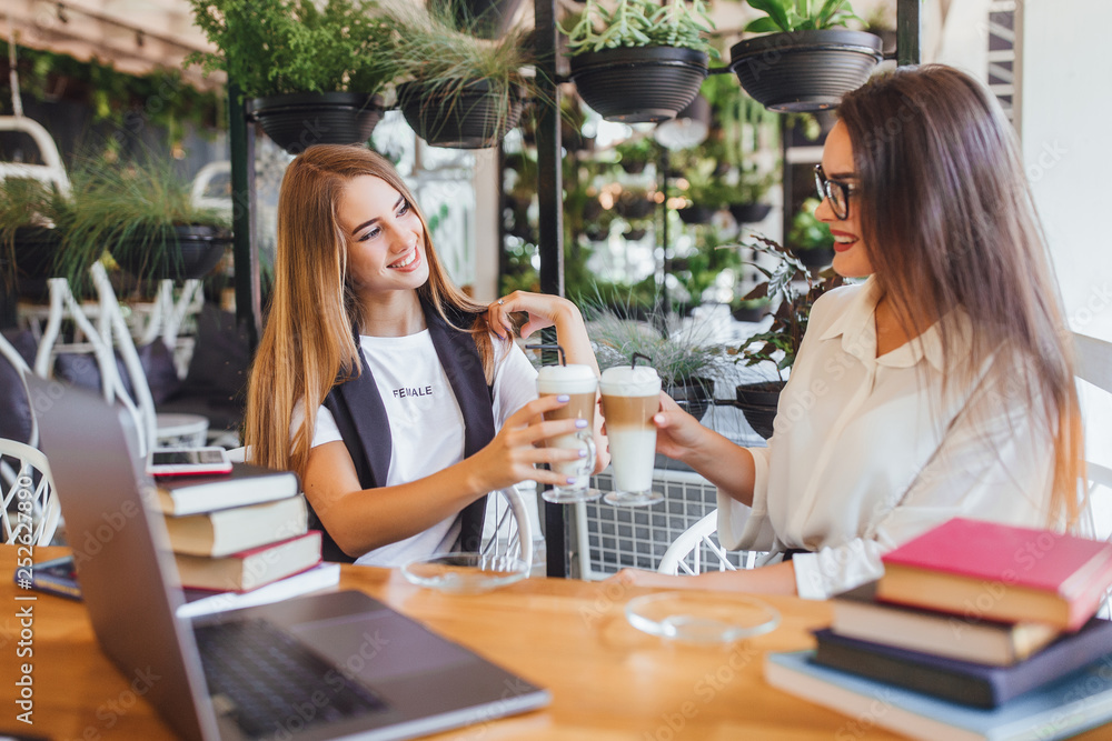 Two young beautiful girls drinking latte in the cafe during coffee break