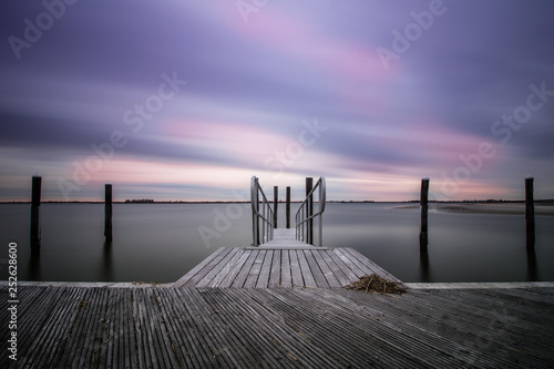 An empty peaceful dock within a marina as clouds streak across the sky. Still water, serene and calm scene