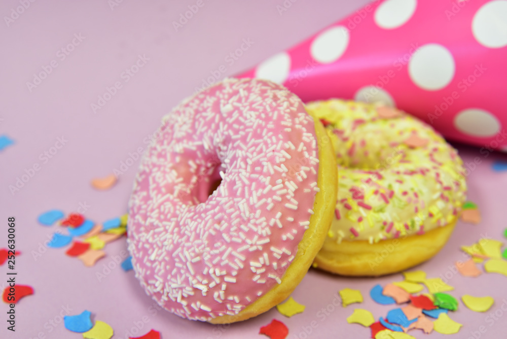 ein gelber und ein rosa donut mit konfetti und einem geburtstagshut vor rosa hintergrund