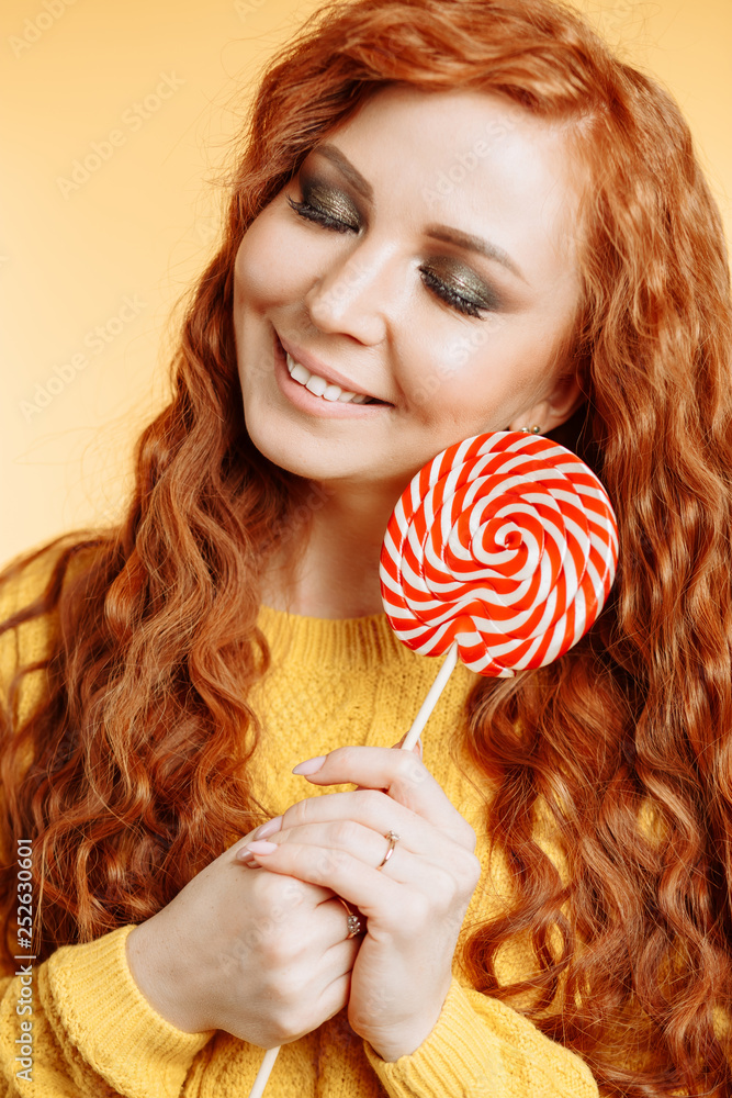 Cheerful curly redhead woman holding a red white lollipop