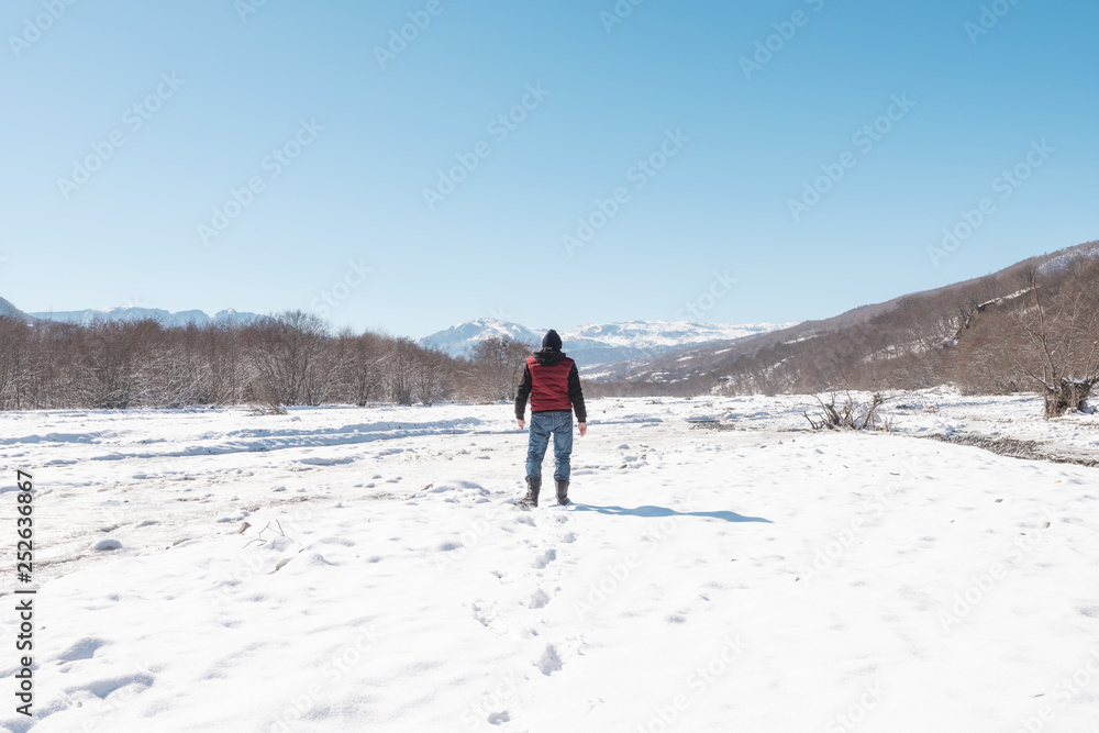 A lone man walks along the frozen bed of a mountain river