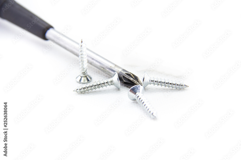 four screws next to the Phillips screwdriver on white background four screws next to the Phillips screwdriver on white background