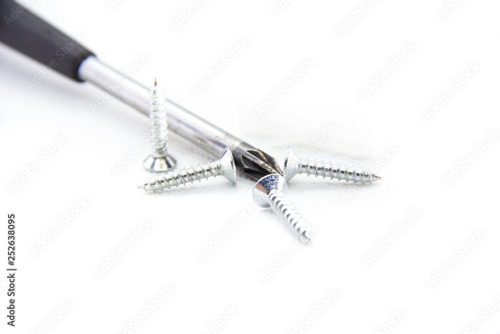 four screws next to the Phillips screwdriver on white background four screws next to the Phillips screwdriver on white background