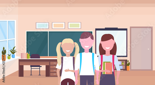 pupils with backpack holding books schoolboy and schoolgirls standing together education knowledge concept male female characters portrait school classroom interior horizontal