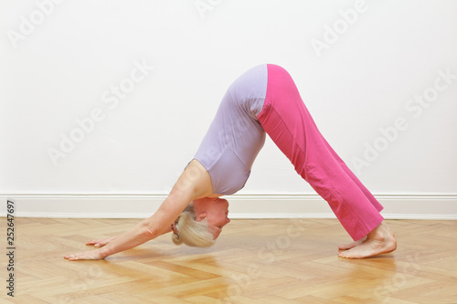 Fototapeta Senior woman with gray hair doing yoga exercise at home in front of a white wall