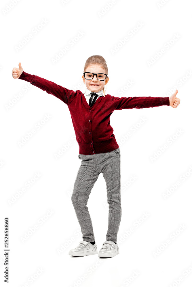 Beautiful little girl dressed like a School girl - in white shirt, red blouse and gray pants, rounded glasses standing near white wall and posing thumbs-up like model. Beautiful little girl dressed like a School girl - in white shirt, red blouse and gray pants, rounded glasses standing near white wall and posing thumbs-up like model.