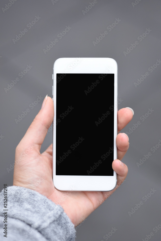 Hand of a woman holding phone white phone black empty screen outside with neutral grey background Hand of a woman holding phone white phone black empty screen outside with neutral grey background