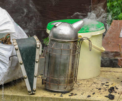 Beekeping smoker lit and smoking next to a pile of fuel