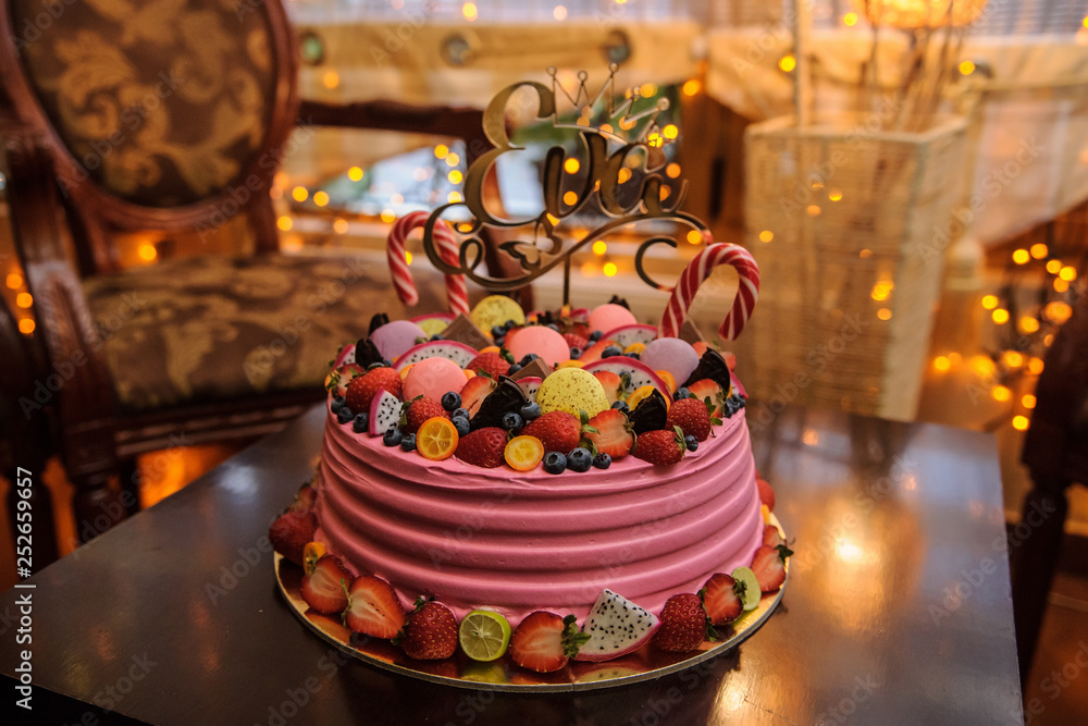 close up photo of a pink bithday cake decorated with fruits, candies and macarons for a little girl