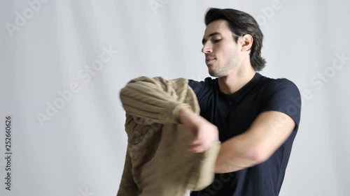 Handsome fit young man dressing, putting on a sweater ove a black t-shirt. Shot in studio on light background