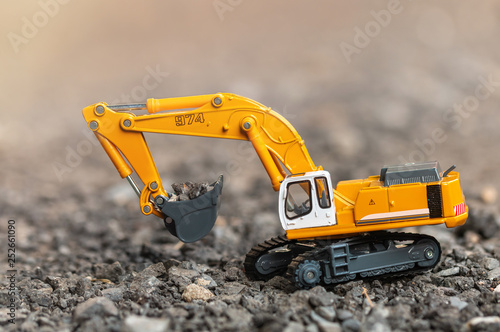 Yellow excavator model toy performs excavation work and load a gravel stone on a construction site. (Image stacking technique)