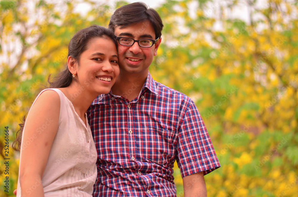 Young Indian couple smiling standing against yellow golden shower amaltas leaves during summer autumn weather in Delhi, India Young Indian couple smiling standing against yellow golden shower amaltas leaves during summer autumn weather in Delhi, India