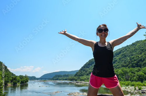 Woman stands with arms raised  from Maryland Heights of the Potomac River from Harpers Ferry West Virginia  concept for freedom and happiness  wearing running activewear clothing