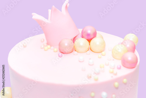 pink cake for a girl with a decoration in the form of a crown and balls on an isolated background