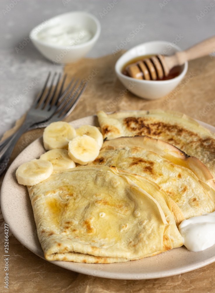 Thin pancakes or crepes with natural yogurt, honey and banana on a plate. Light concrete background. Copy space. Thin pancakes or crepes with natural yogurt, honey and banana on a plate. Light concrete background. Copy space.