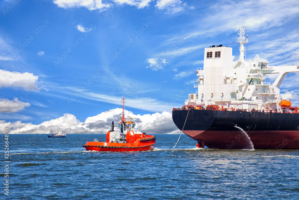 Tanker ship with escorting tug leaving port.