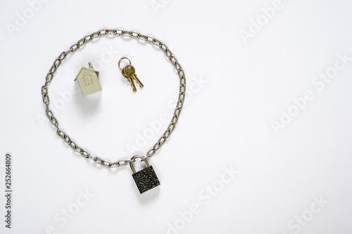 Imitation of a house made of metal fenced with a metal chain with a lock and keys on a white background.