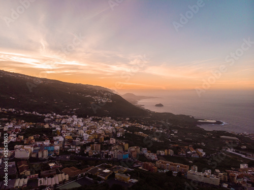 sunset in Tenerife North with the cliff and a rock in the middle of the sea and a town. Picture by drone