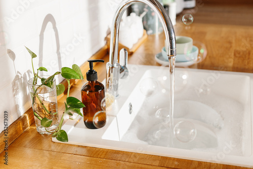 White sink glass soap dispenser bamboo dish washing brush wooden countertop and white ceramic brick tile background